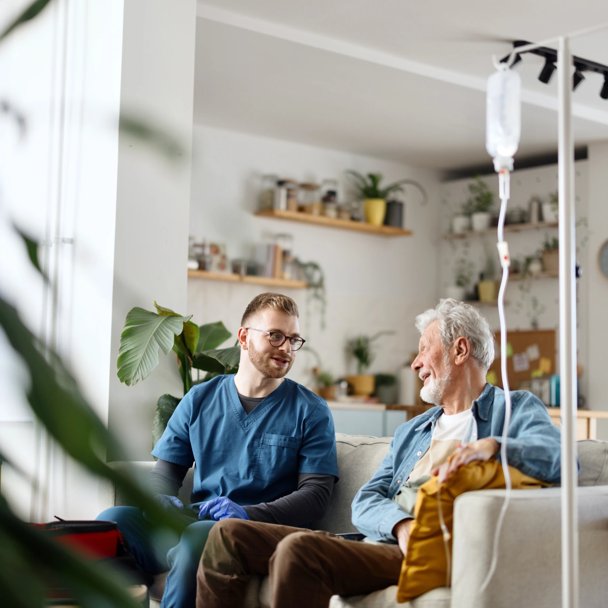 Pflegekraft betreut einen älteren Patienten zuhause im Wohnzimmer